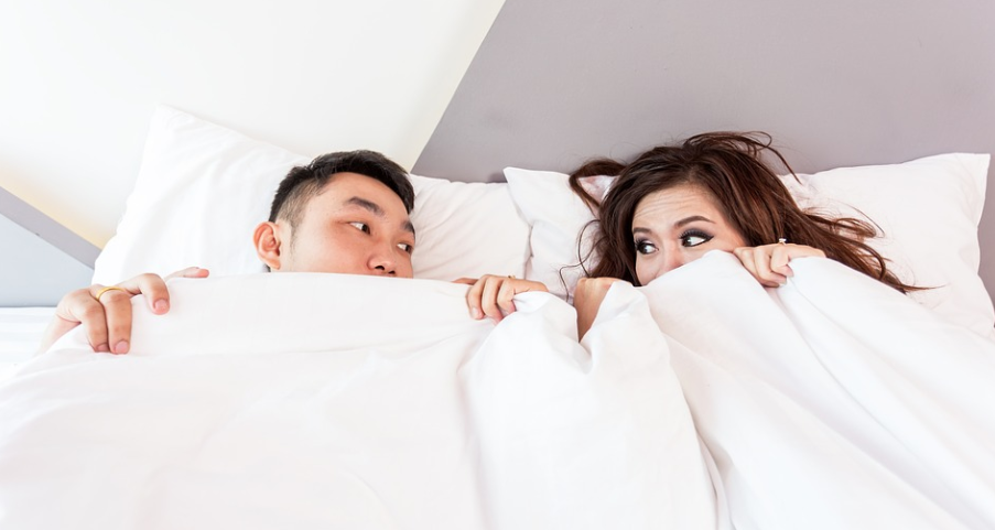 a couple in bed looking at each other while hiding their whole body in a comforter