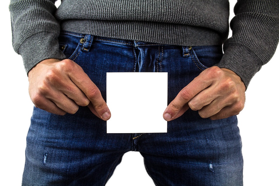 man wearing longsleeve and blue jeans holding a white paper in front of his private part